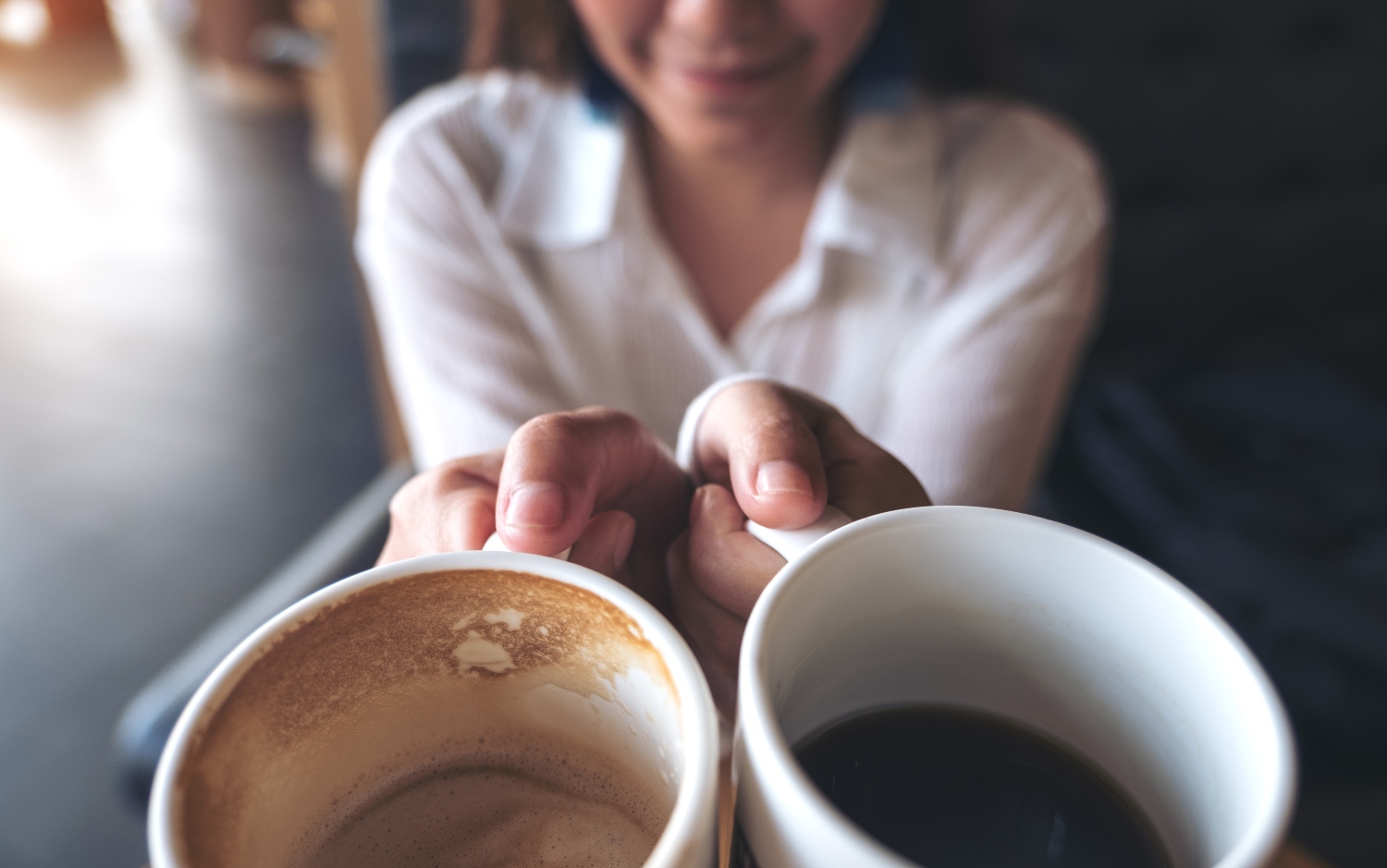 Close up image of a woman holding two white coffee mugs in cafe