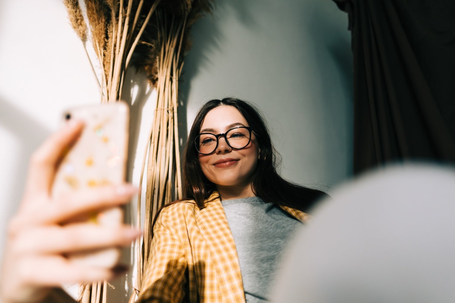 Young happy woman holding smartphone looking on cell using mobile phone technology at home