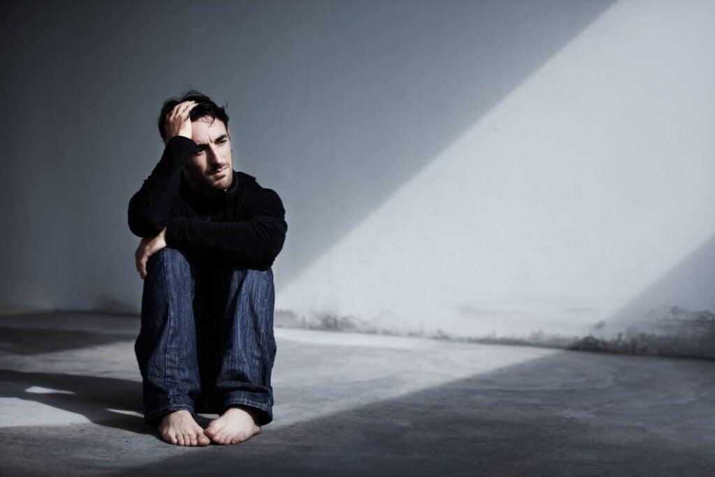 A young man sitting on the ground with his hand on his head