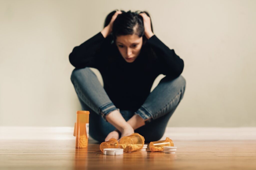 Young millennial woman looking depressed sitting next to a bunch of pill bottles, trauma and addiction concept