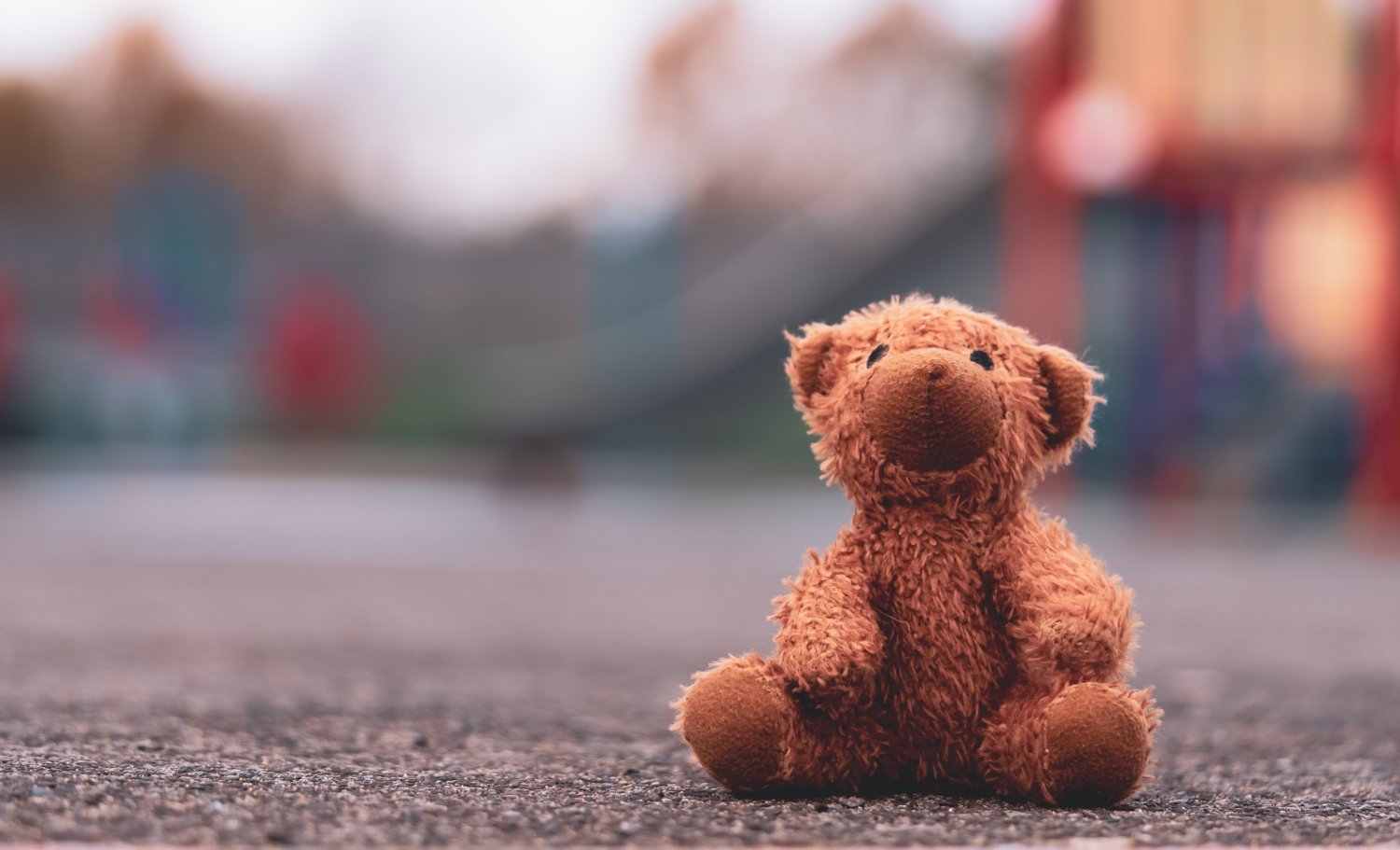 Lost teddy bear toy lying on playground floor, childhood concept