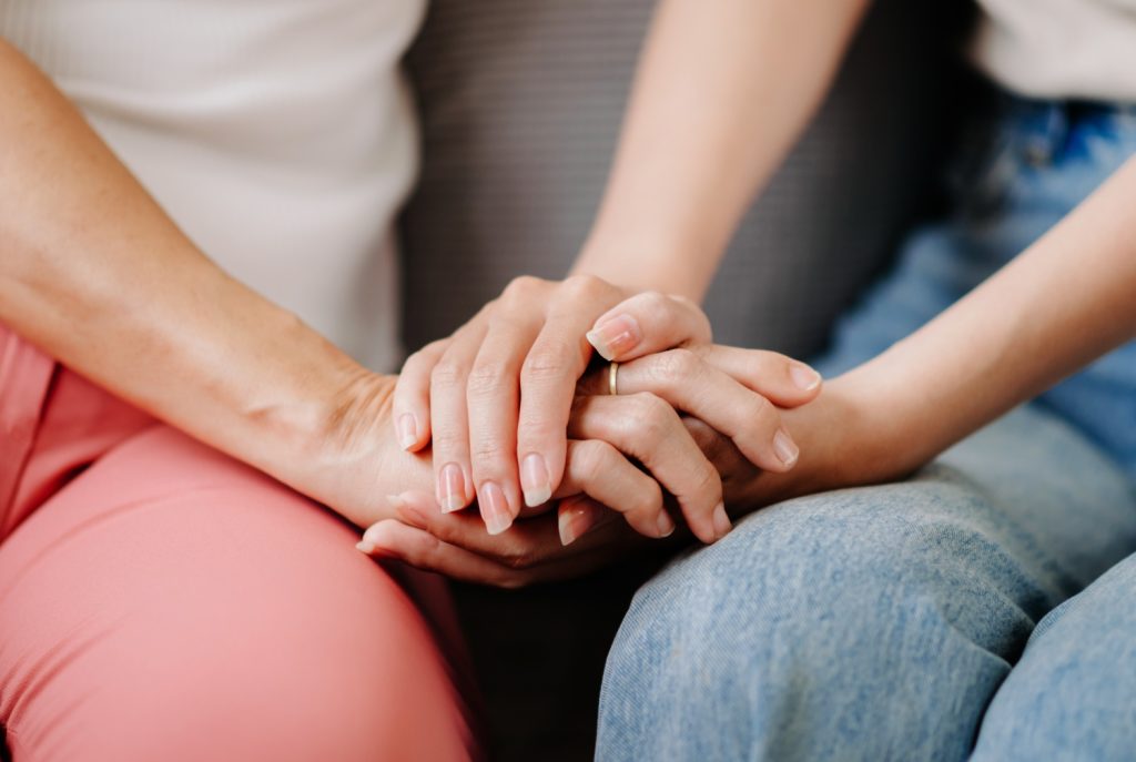 focused shot of mother's and adult daughter's hands, holding each other, concept of family support