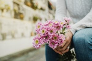 Faceless woman with flowers bouquet in hands sitting in cemetery, concept of grief